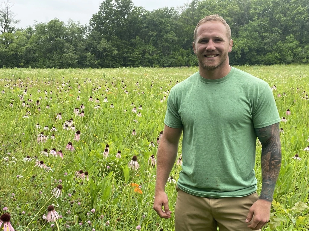 Portrait image of Dustin Williams standing in front of a field of flowers and grass